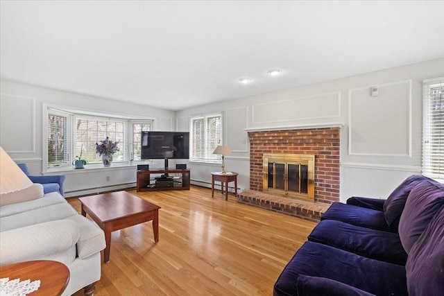 living room with a baseboard heating unit, a healthy amount of sunlight, baseboard heating, and light wood-type flooring