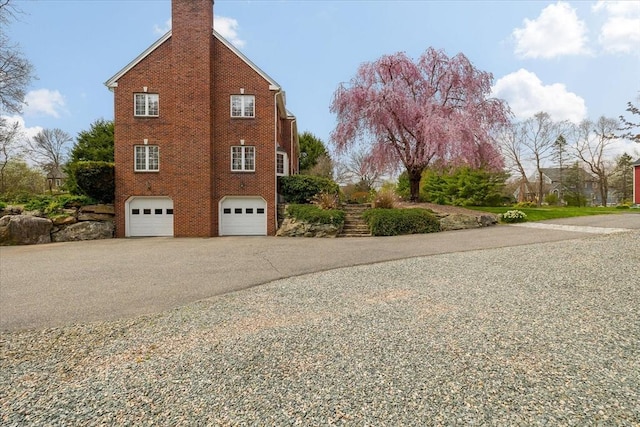 view of side of property with a garage, aphalt driveway, a chimney, brick siding, and stairs
