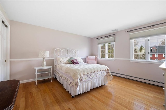 bedroom with visible vents, wood finished floors, baseboards, a closet, and a baseboard heating unit