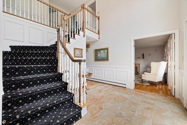 staircase featuring a wainscoted wall, a high ceiling, baseboard heating, and stone finish flooring