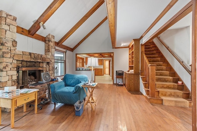 living room featuring high vaulted ceiling, a stone fireplace, stairs, beamed ceiling, and wood-type flooring