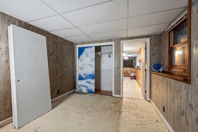 unfurnished room featuring wood walls, a paneled ceiling, and baseboards