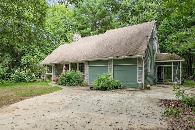 view of front of house featuring a garage, a sunroom, a chimney, and concrete driveway