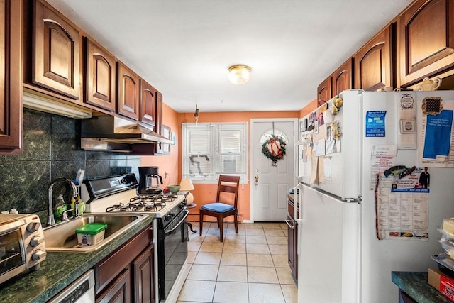 kitchen with freestanding refrigerator, black gas stove, under cabinet range hood, a sink, and decorative backsplash