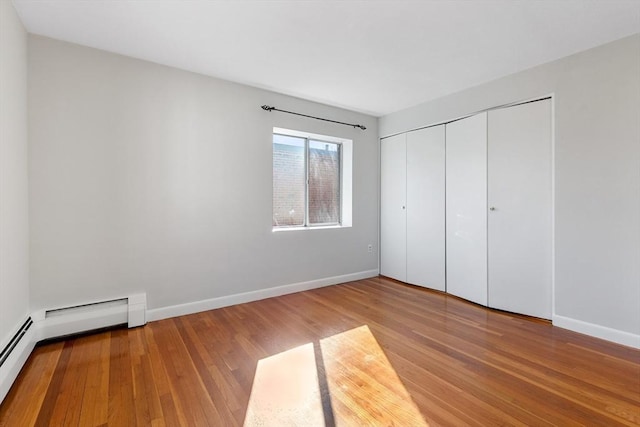 unfurnished bedroom featuring hardwood / wood-style flooring, a baseboard radiator, and a closet