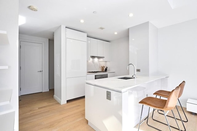 kitchen with a breakfast bar, stainless steel gas cooktop, sink, light hardwood / wood-style flooring, and white cabinetry