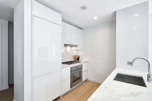 kitchen featuring sink, light stone counters, light hardwood / wood-style flooring, white cabinets, and appliances with stainless steel finishes