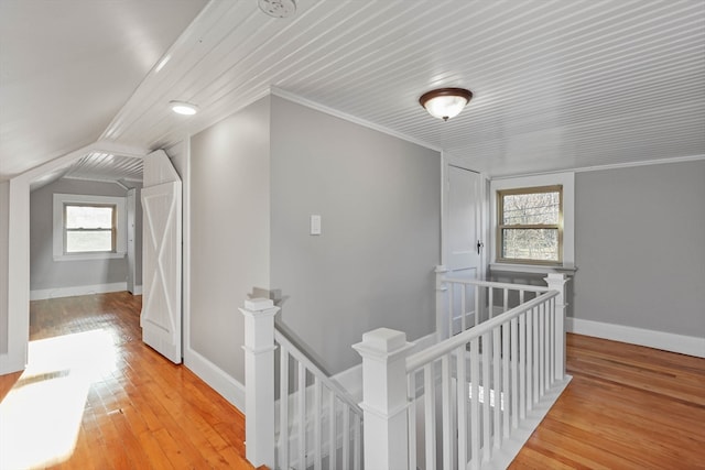 corridor featuring light wood-type flooring, vaulted ceiling, a healthy amount of sunlight, and crown molding