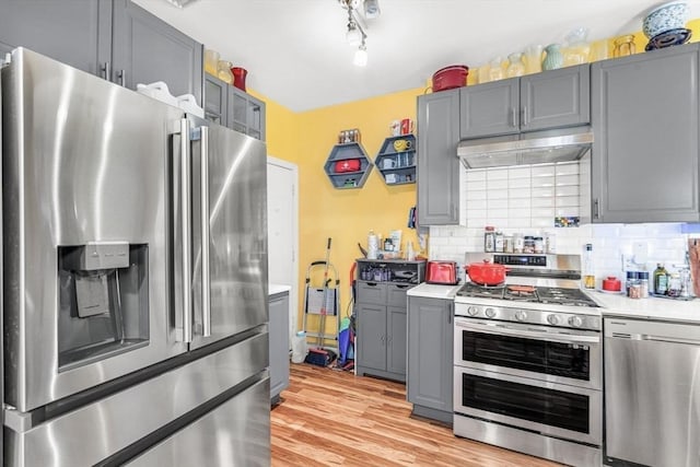 kitchen with gray cabinets, backsplash, stainless steel appliances, light hardwood / wood-style floors, and exhaust hood