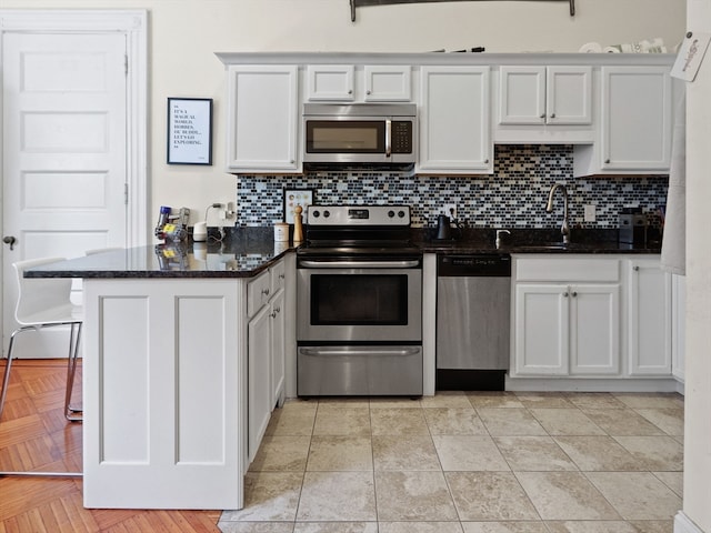 kitchen with white cabinetry, kitchen peninsula, appliances with stainless steel finishes, and dark stone counters