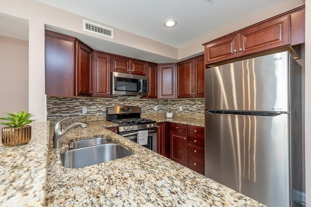 kitchen featuring stainless steel appliances, sink, backsplash, and light stone counters