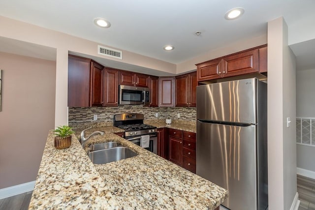 kitchen with sink, light stone counters, kitchen peninsula, stainless steel appliances, and backsplash