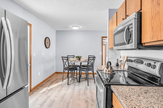 kitchen with light wood finished floors, backsplash, appliances with stainless steel finishes, a textured ceiling, and baseboards