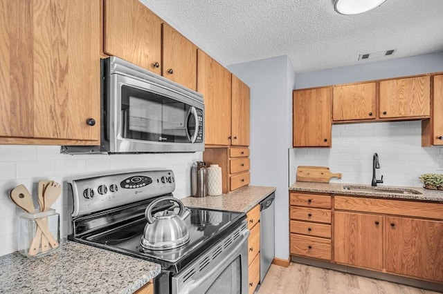 kitchen featuring light stone counters, a sink, appliances with stainless steel finishes, light wood finished floors, and tasteful backsplash