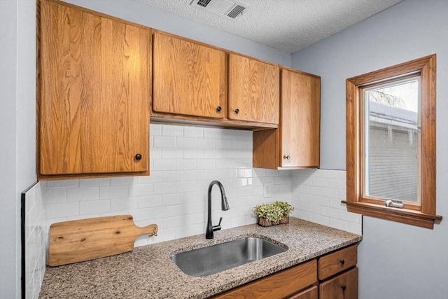 kitchen with tasteful backsplash, visible vents, a sink, a textured ceiling, and light stone countertops