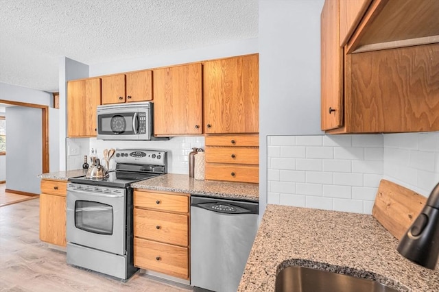 kitchen featuring light wood-style flooring, light stone countertops, stainless steel appliances, a textured ceiling, and backsplash