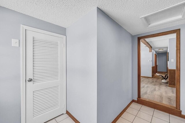 hallway with a textured ceiling, light tile patterned floors, and attic access