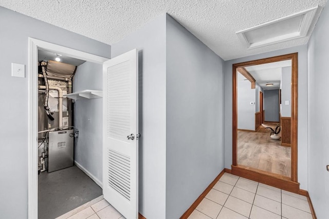 hall featuring a textured ceiling, light tile patterned floors, baseboards, heating unit, and attic access