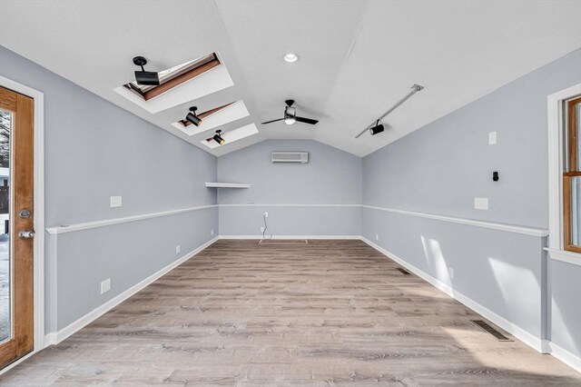 spare room featuring ceiling fan, vaulted ceiling with skylight, wood finished floors, visible vents, and a wall mounted air conditioner