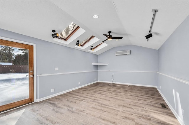 bonus room with vaulted ceiling with skylight, wood finished floors, visible vents, baseboards, and a wall mounted air conditioner