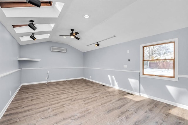 spare room featuring vaulted ceiling with skylight, baseboards, ceiling fan, wood finished floors, and a wall mounted air conditioner