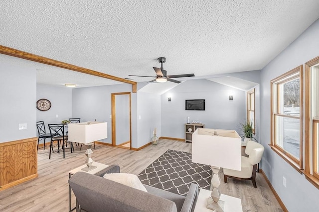 living area with light wood finished floors, ceiling fan, vaulted ceiling, and a textured ceiling