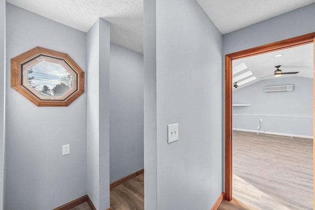 corridor featuring an AC wall unit, vaulted ceiling, a textured ceiling, wood finished floors, and baseboards