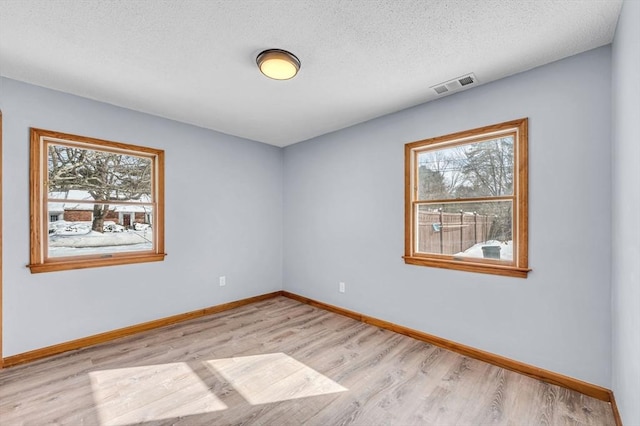 unfurnished room featuring light wood-type flooring, a wealth of natural light, visible vents, and baseboards