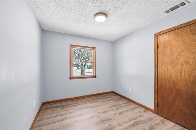 unfurnished room with light wood-style floors, baseboards, visible vents, and a textured ceiling