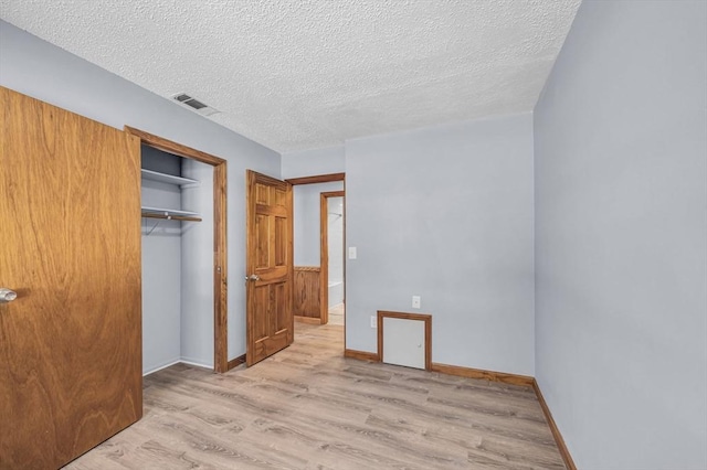 unfurnished bedroom featuring a closet, visible vents, light wood-style floors, a textured ceiling, and baseboards