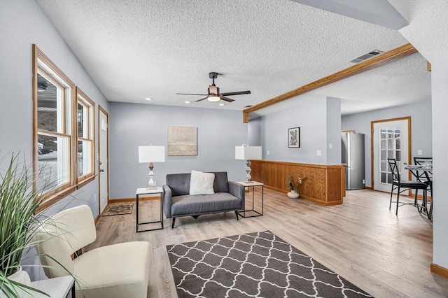 living area featuring light wood-style floors, visible vents, ceiling fan, and a textured ceiling