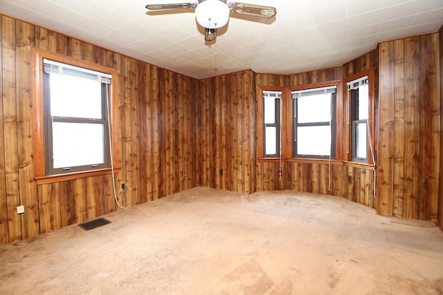 carpeted spare room with visible vents, a ceiling fan, and wooden walls