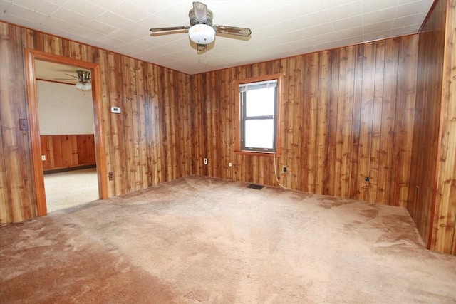 unfurnished room with carpet floors, wood walls, and ceiling fan