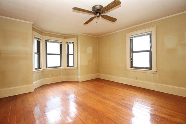 spare room with light wood-type flooring, a ceiling fan, baseboards, and crown molding