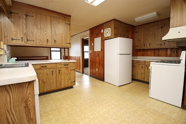 kitchen featuring wood walls, white appliances, light countertops, brown cabinets, and a sink