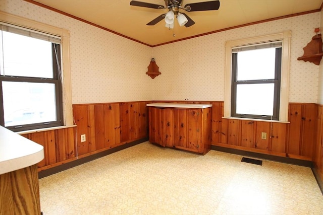 unfurnished room featuring ceiling fan, visible vents, crown molding, wainscoting, and wooden walls