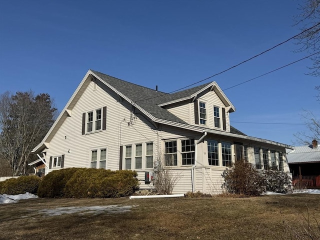 view of side of property featuring a lawn and a shingled roof