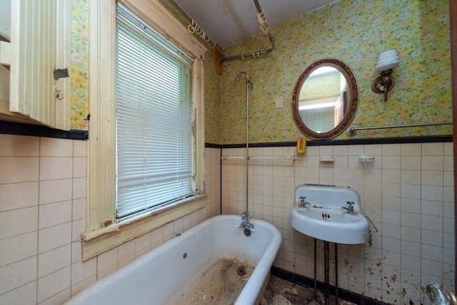 bathroom with a tub to relax in, plenty of natural light, wallpapered walls, tile walls, and wainscoting