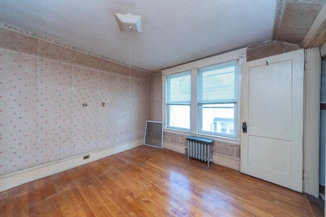 empty room featuring radiator heating unit, wallpapered walls, light wood-style flooring, and baseboards