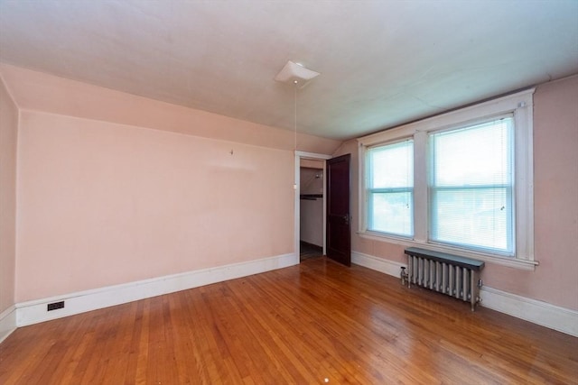 unfurnished bedroom with radiator heating unit, wood finished floors, baseboards, and vaulted ceiling