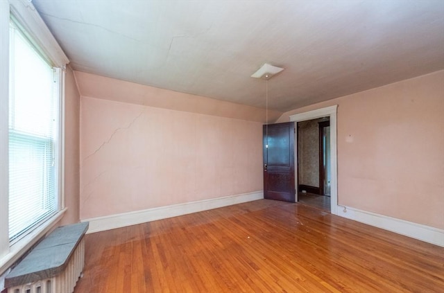 spare room with healthy amount of natural light, hardwood / wood-style flooring, baseboards, and radiator heating unit