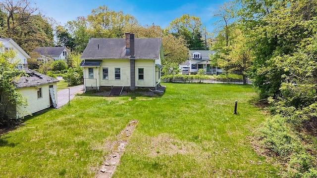 rear view of property with a chimney, a lawn, and view of scattered trees