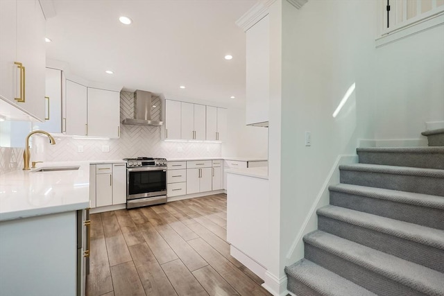 kitchen featuring light wood-type flooring, stainless steel gas range oven, wall chimney exhaust hood, sink, and white cabinets