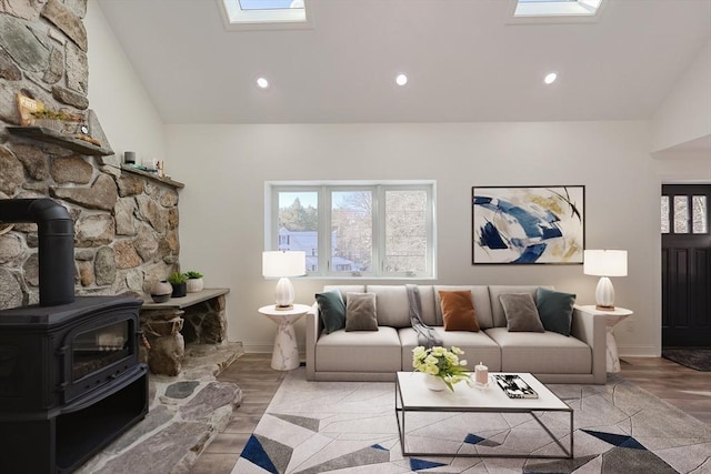 living room with light hardwood / wood-style flooring, a wood stove, and lofted ceiling with skylight