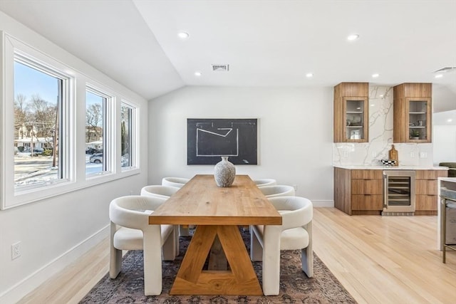 dining space featuring vaulted ceiling, wine cooler, and light wood-type flooring