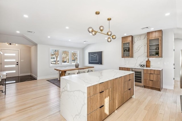 kitchen featuring a kitchen island, beverage cooler, hanging light fixtures, light stone counters, and light hardwood / wood-style flooring