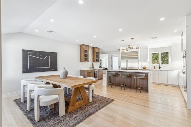 dining space featuring lofted ceiling, sink, beverage cooler, and light hardwood / wood-style floors