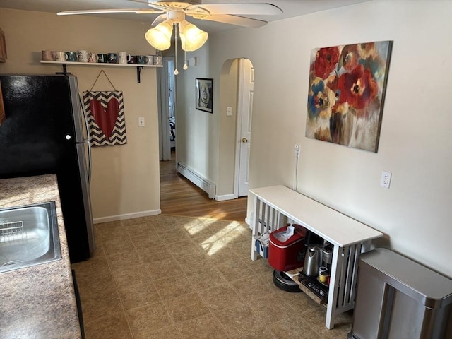 kitchen featuring arched walkways, a baseboard heating unit, freestanding refrigerator, a ceiling fan, and baseboards