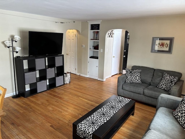 living area featuring arched walkways, baseboards, and wood finished floors