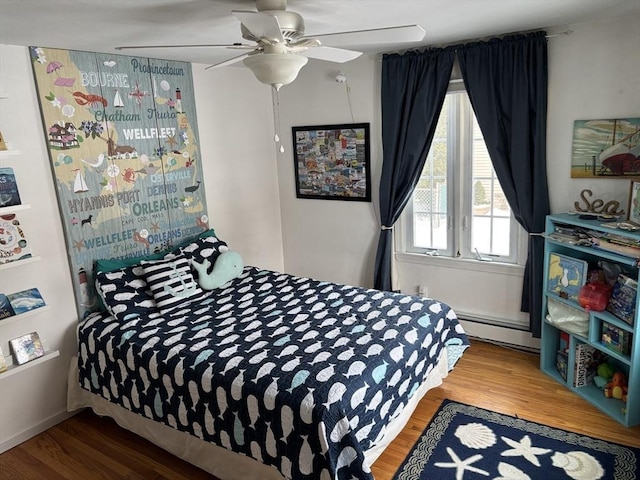 bedroom with a baseboard heating unit, wood finished floors, and a ceiling fan